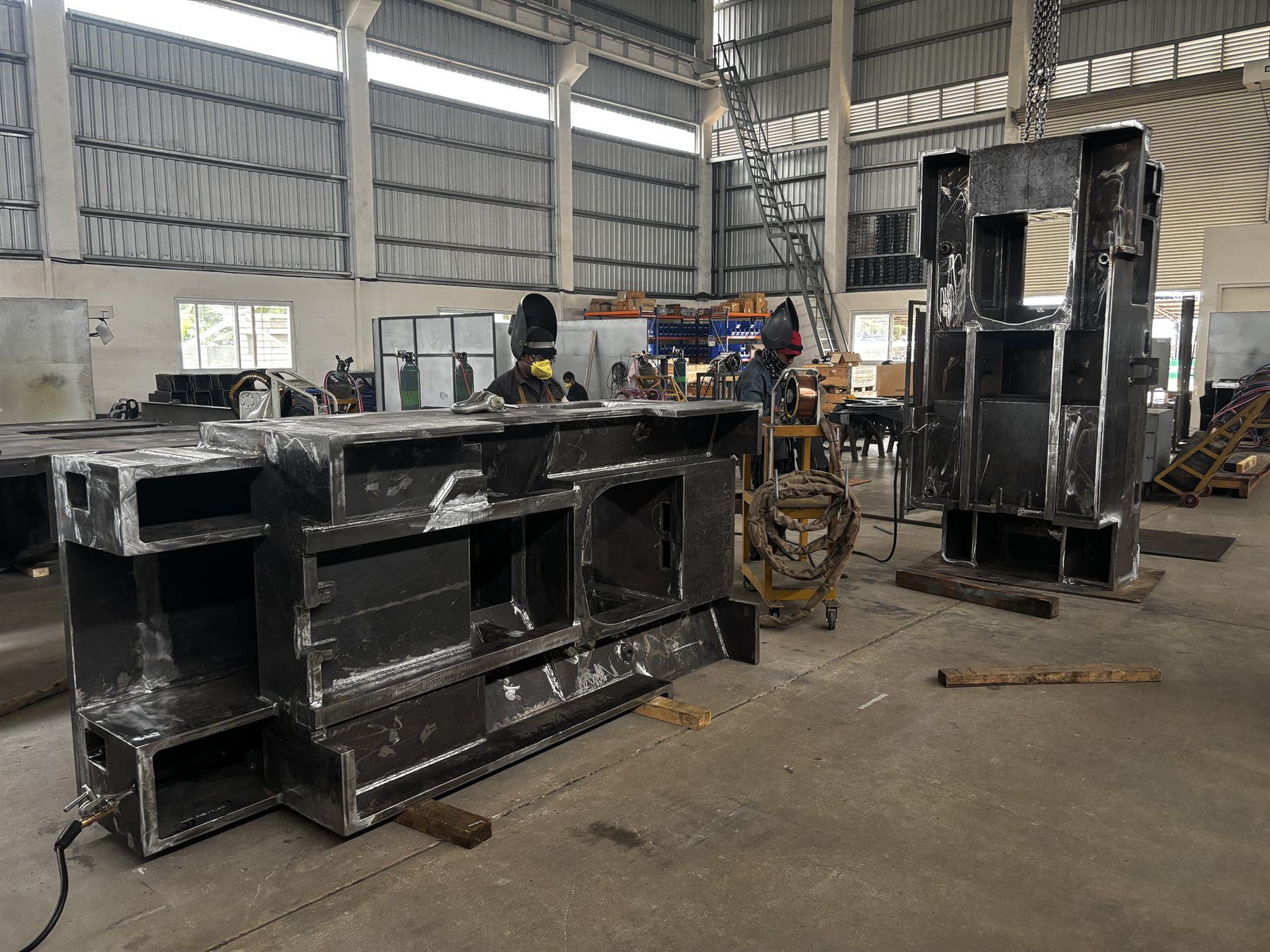 Welders working on heavy machine base weldments in the fabrication bay